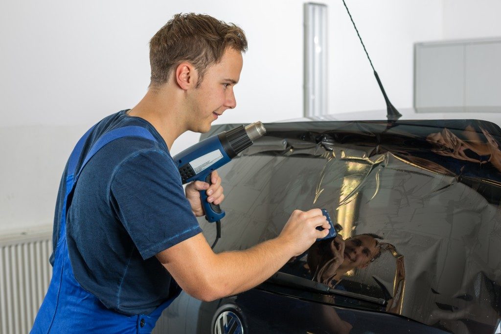 Worker in garage tinting a car window with tinted foil or film