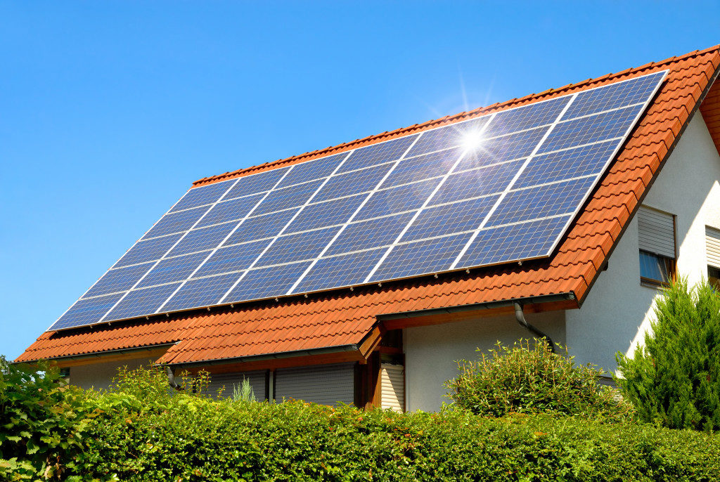 Solar panel on a red roof reflecting the sun and the cloudless blue sky