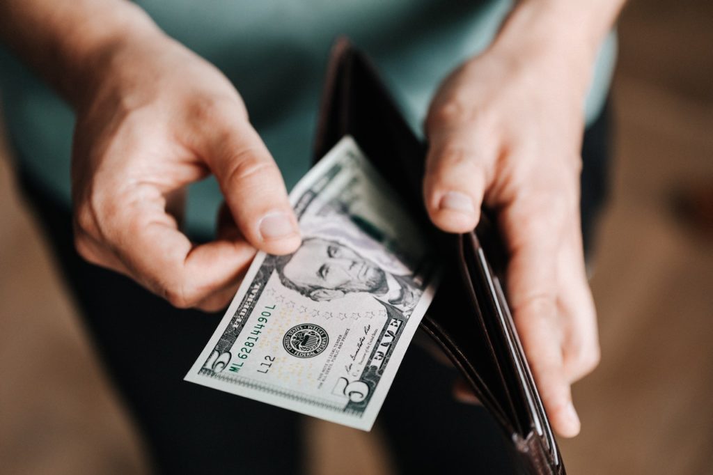 person taking a five dollar bill from his wallet