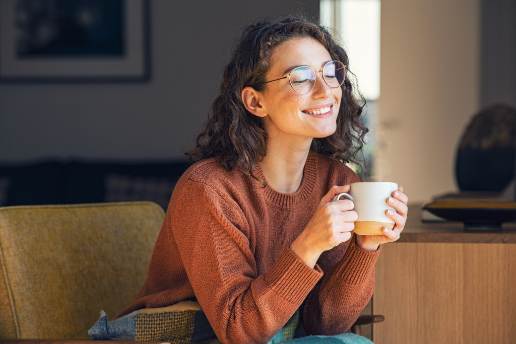 Happy young woman drinking coffee in the living room of her home.