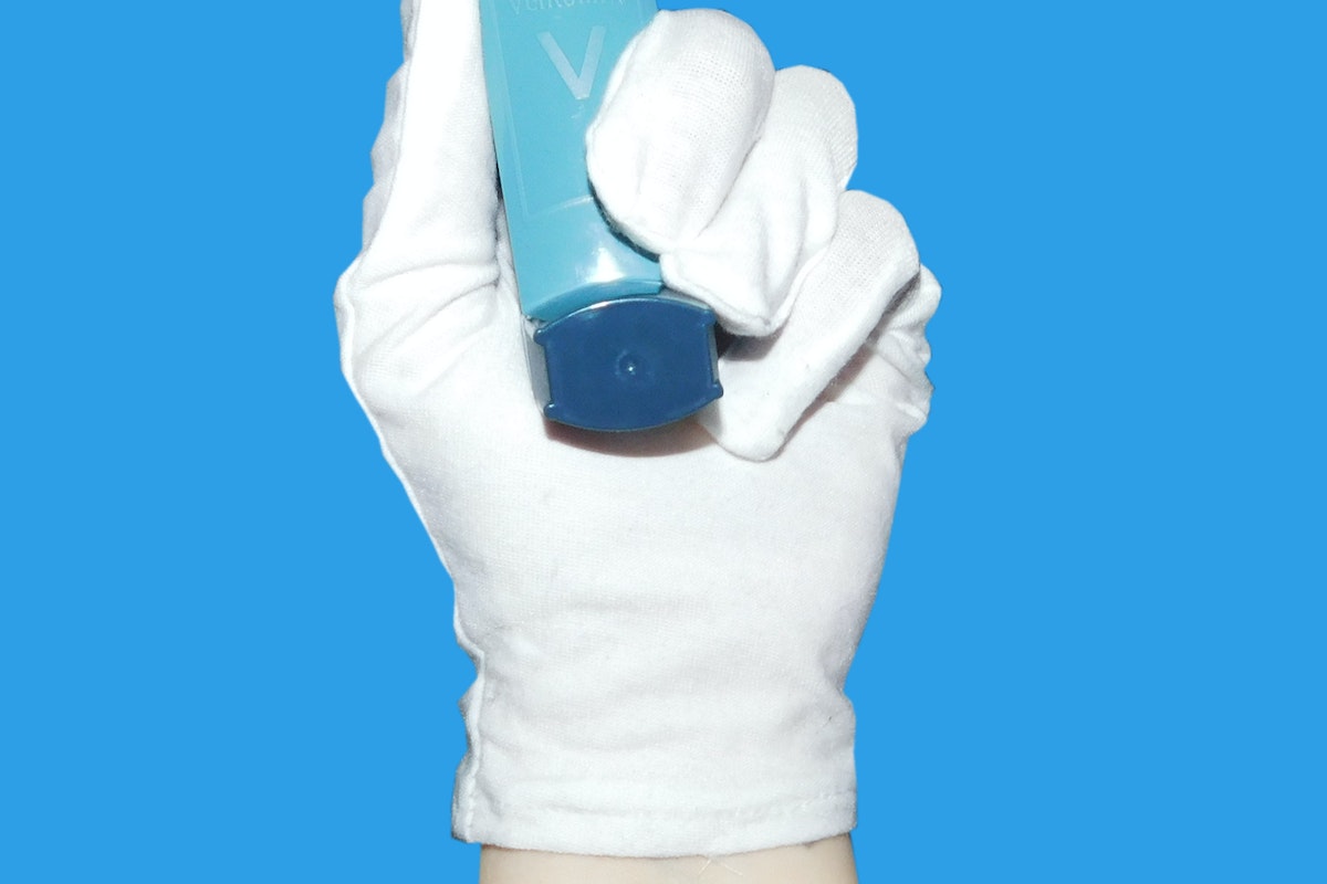 A Hand Wearing White Gloves Holding an Inhaler